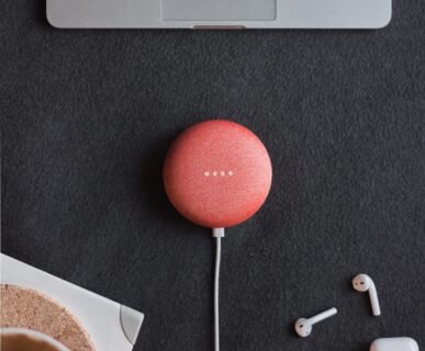 Photography of coral Google Home Mini on black surface beside Apple AirPods